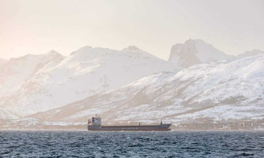 Backlit shot of a vessel, the sea and the mountains of Kvaløya